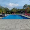 Large backyard pool on sunny day with Cambridge paver patio, waterfalls, and outdoor kitchen/bar area